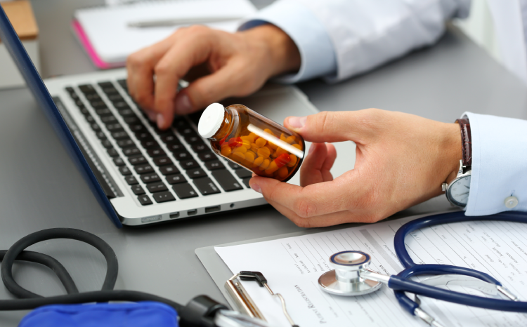 Clinician on laptop holding medication