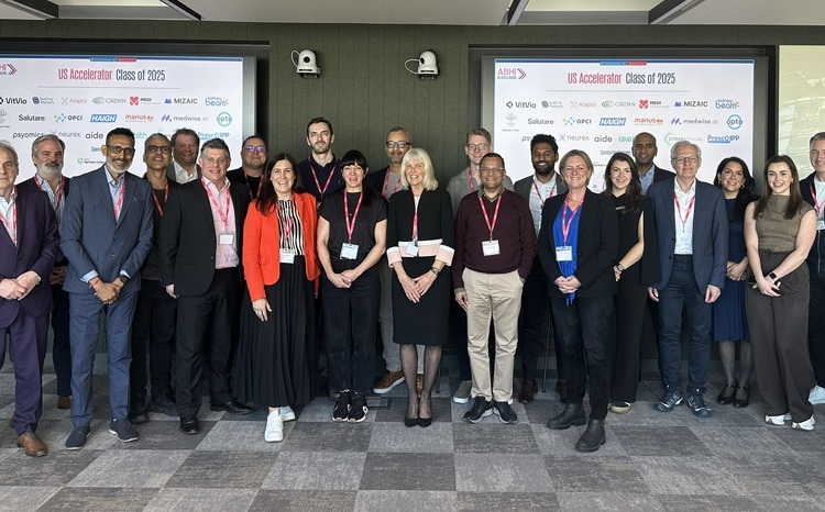 Group photo of the ABHI US Accelerator Class of 2025, featuring representatives from 21 UK digital health companies standing in front of branded display screens showing participant logos.